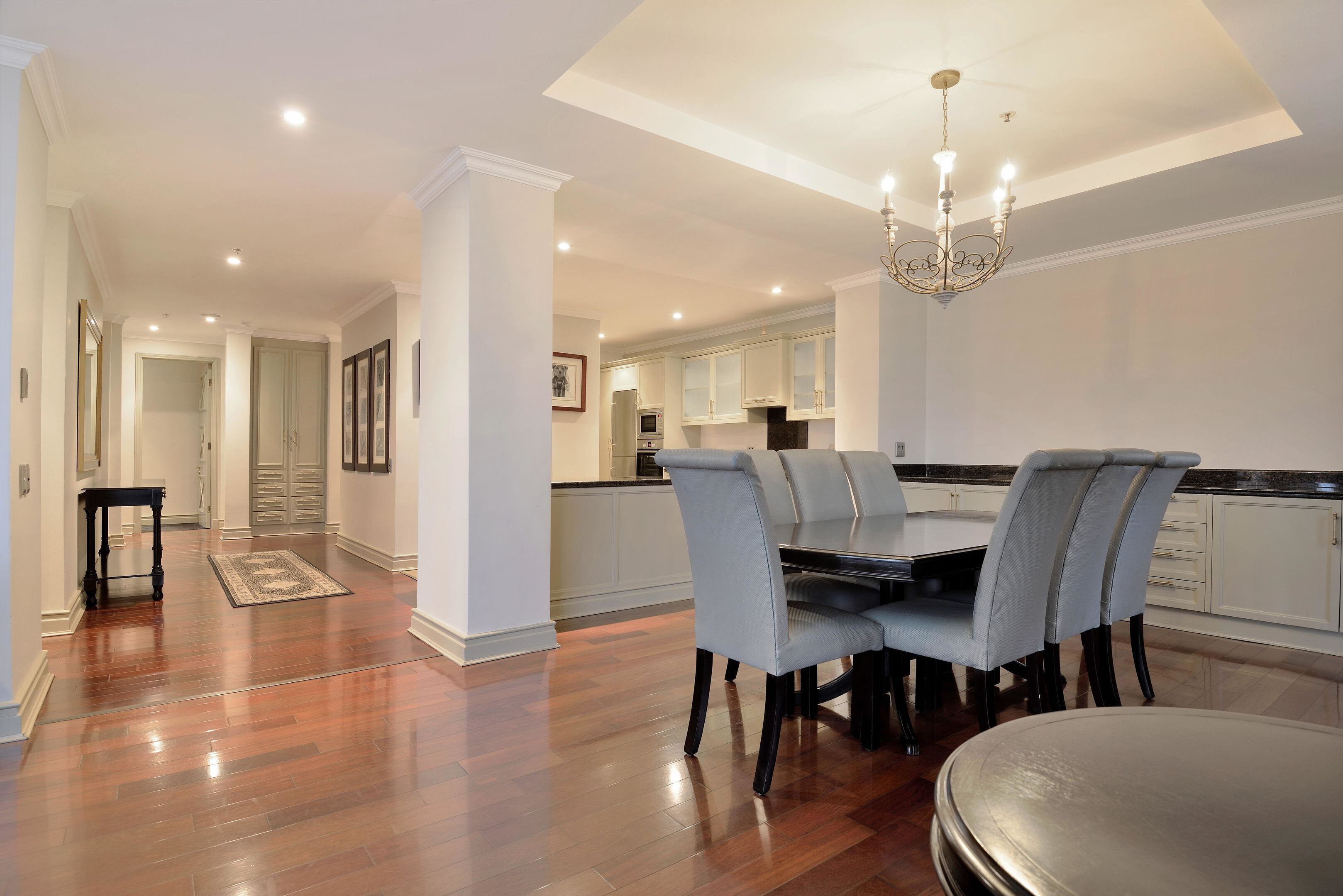 A spacious dining area with a wooden floor, a chandelier, and a view into the kitchen.