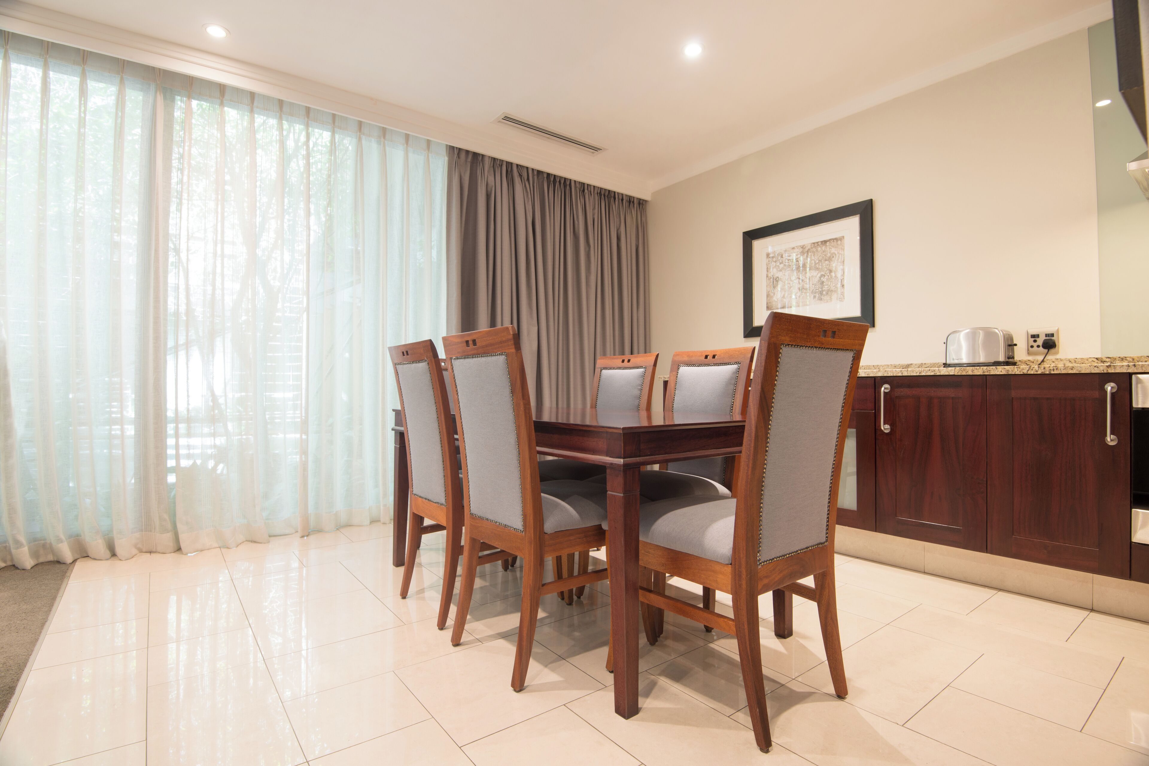 A dining area with a wooden table and chairs, a kitchen with cabinets, and a window with curtains.
