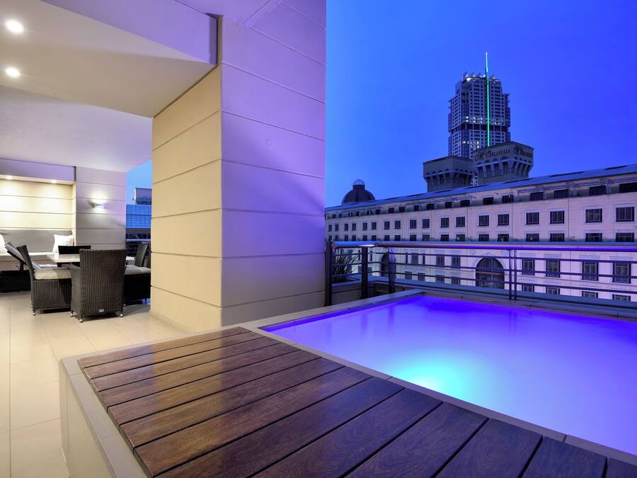 Una terraza moderna en la azotea con piscina, zona de estar y vistas a un paisaje urbano que incluyen un edificio emblemático.
