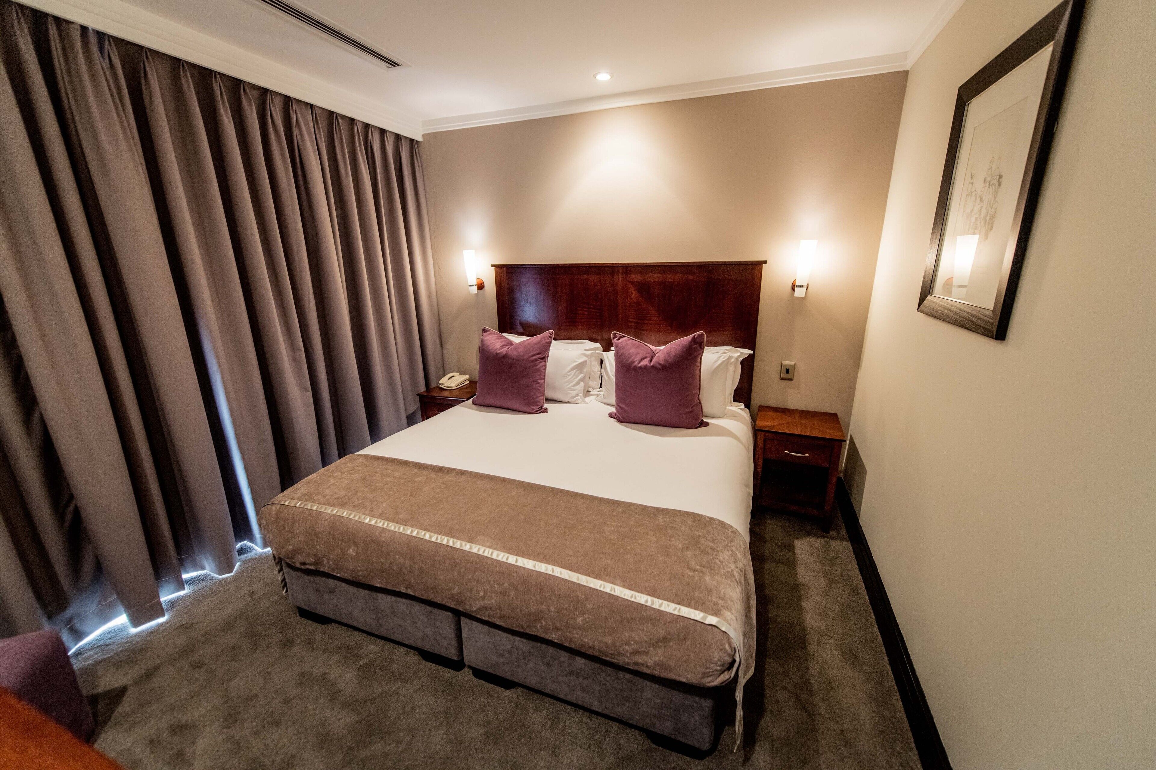A hotel room with a large bed, a wooden headboard, two bedside tables, a nightstand, and a framed picture on the wall.