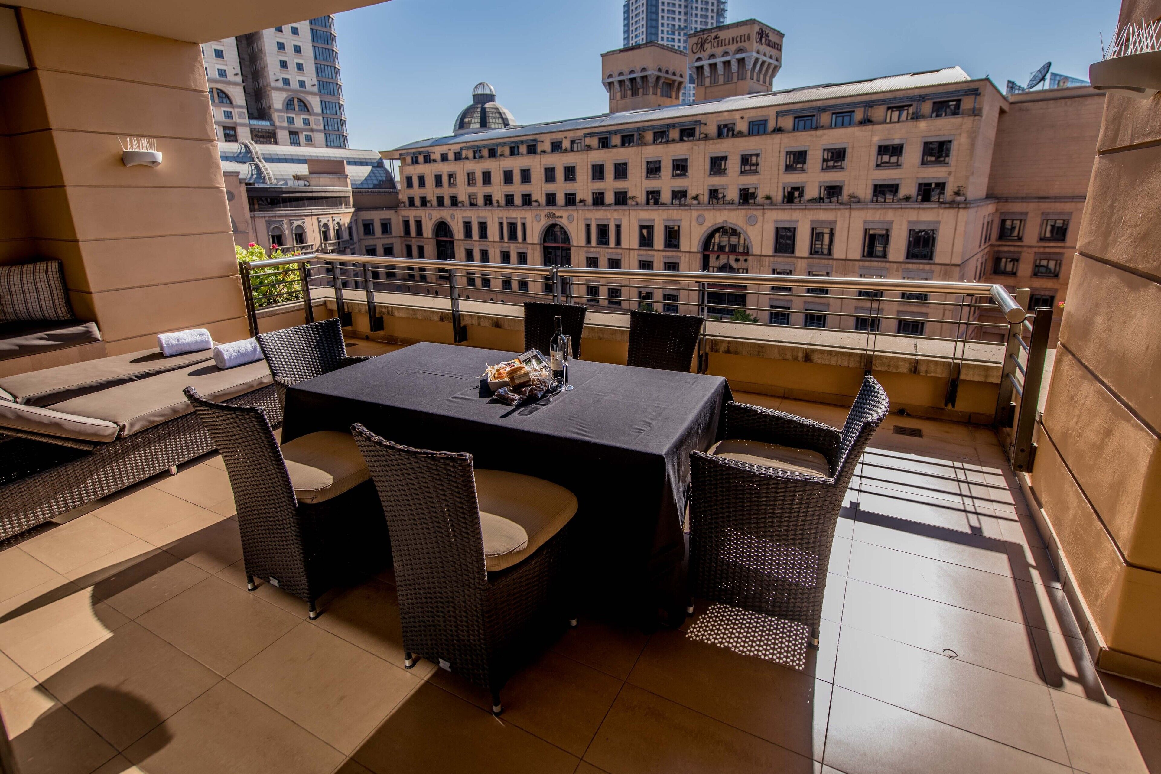 A rooftop terrace with a dining table, wicker chairs, and a view of a historic building.