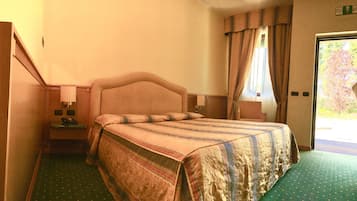A hotel room with a single bed, a nightstand with a lamp, and a view of a tree through the window.