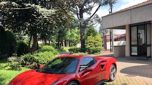 Um carro esportivo vermelho estacionado em área ajardinada, com um edifício ao fundo.