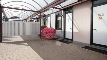 A covered walkway with a white fence, a pink bush, and a door marked with the number 162.