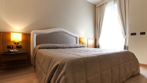 Quarto de hotel com cama grande, luminárias de cabeceira, mesa de cabeceira e janela com cortinas.