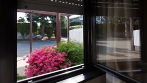 Janela com vista para um jardim, incluindo flores cor-de-rosa e arbustos verdes.