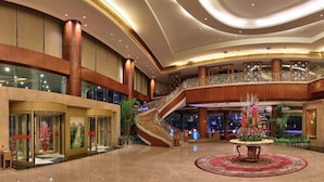 A spacious lobby with a grand staircase, a central decorative fountain, and a high ceiling with recessed lighting.