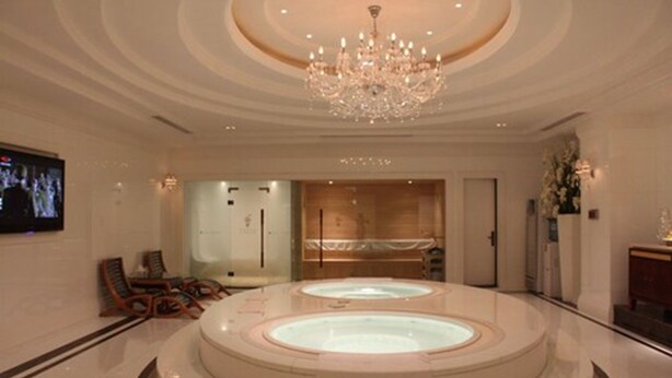 A luxurious lobby with a central circular hot tub, a grand chandelier, and a television screen.