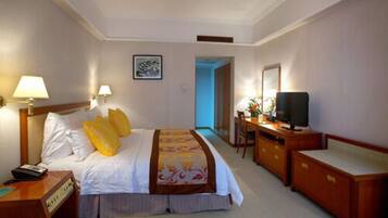 A hotel room with a bed, bedside lamps, a desk with a television, and a dresser.