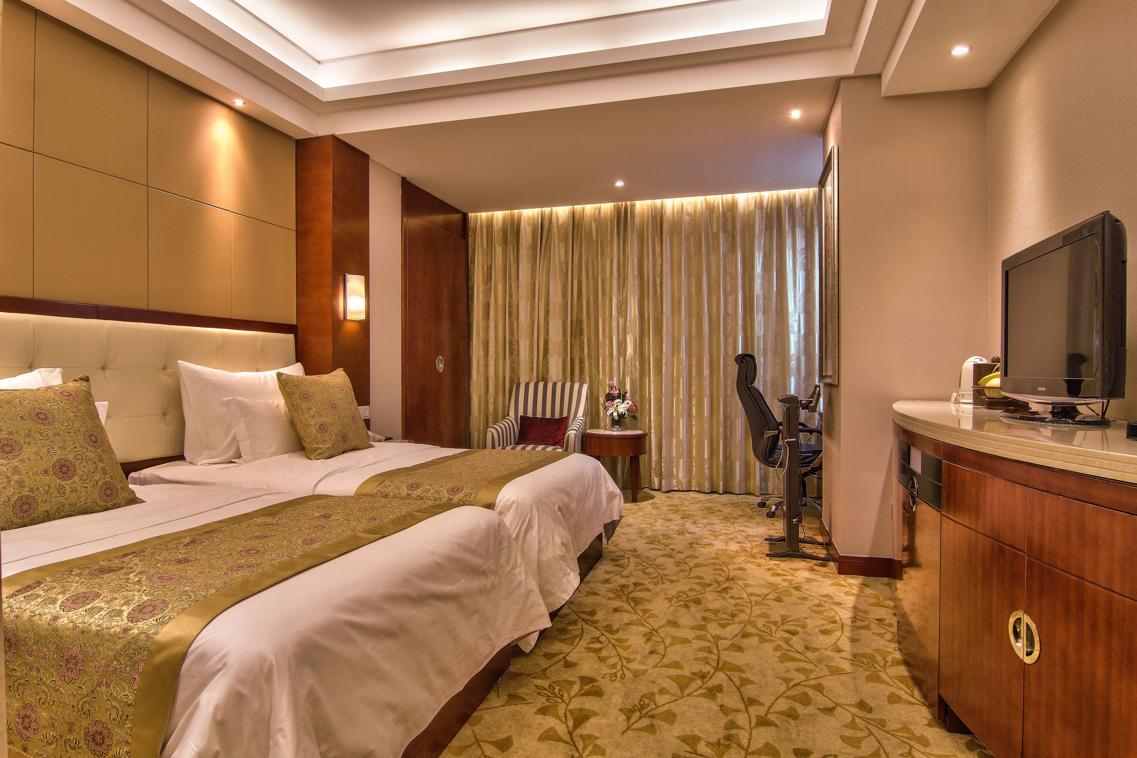 Habitación de hotel con dos camas, televisión, escritorio y baño.