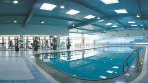 An indoor swimming pool with a tiled floor, ceiling lights, and potted plants.