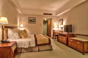 A hotel room with a bed, bedside lamps, a desk with a television, and a chair.