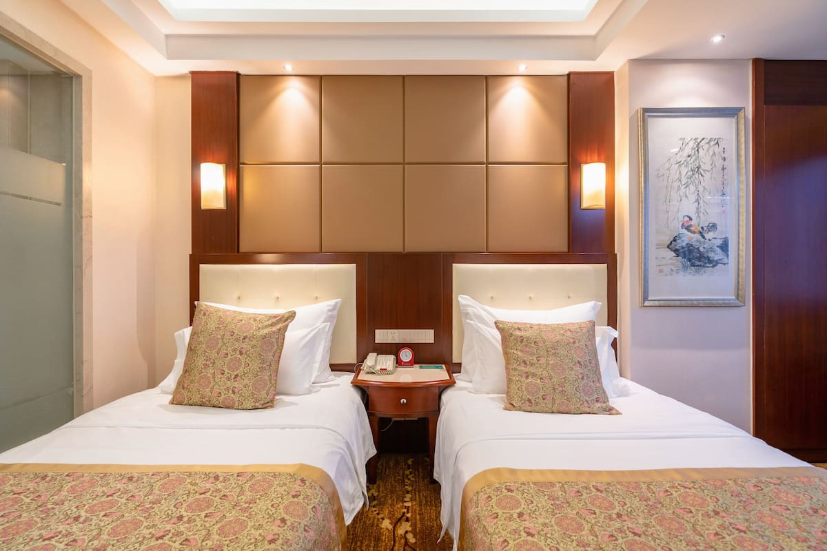 Een hotelkamer met twee bedden, een houten hoofdbord, een nachtkastje met een telefoon en een lijst met kunst aan de muur.