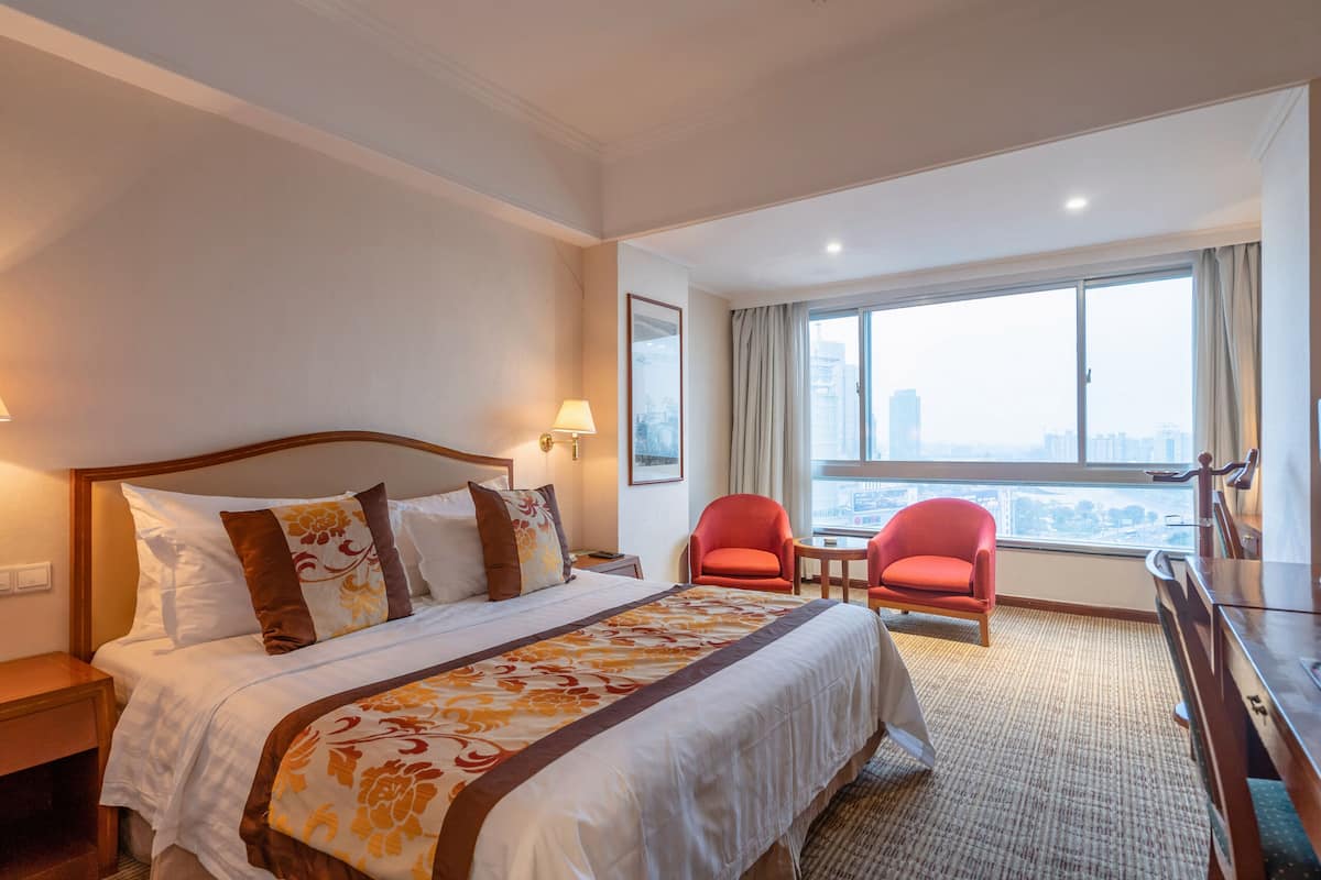 Hotelkamer met een groot bed, twee rode stoelen, een bureau en uitzicht op de stad.