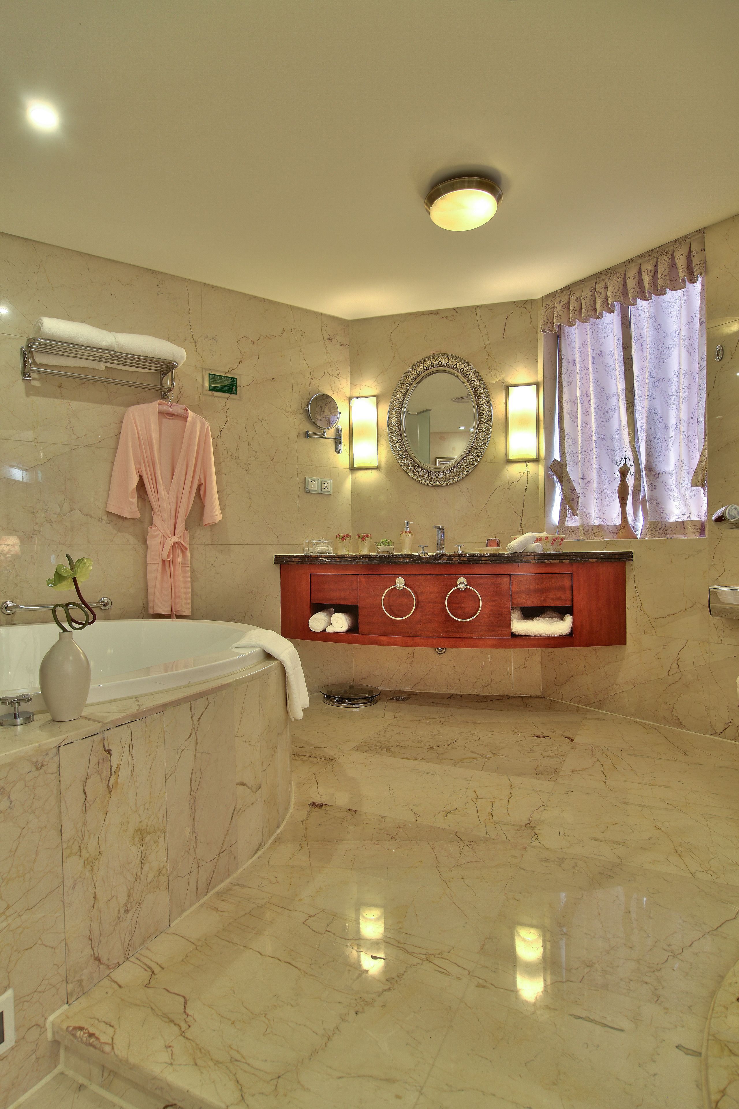 A marble bathroom with a bathtub, vanity, and a robe hanging on the wall.