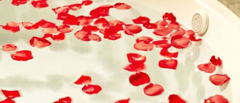 A bathroom with a bathtub filled with water and rose petals, a sink, and toiletries.