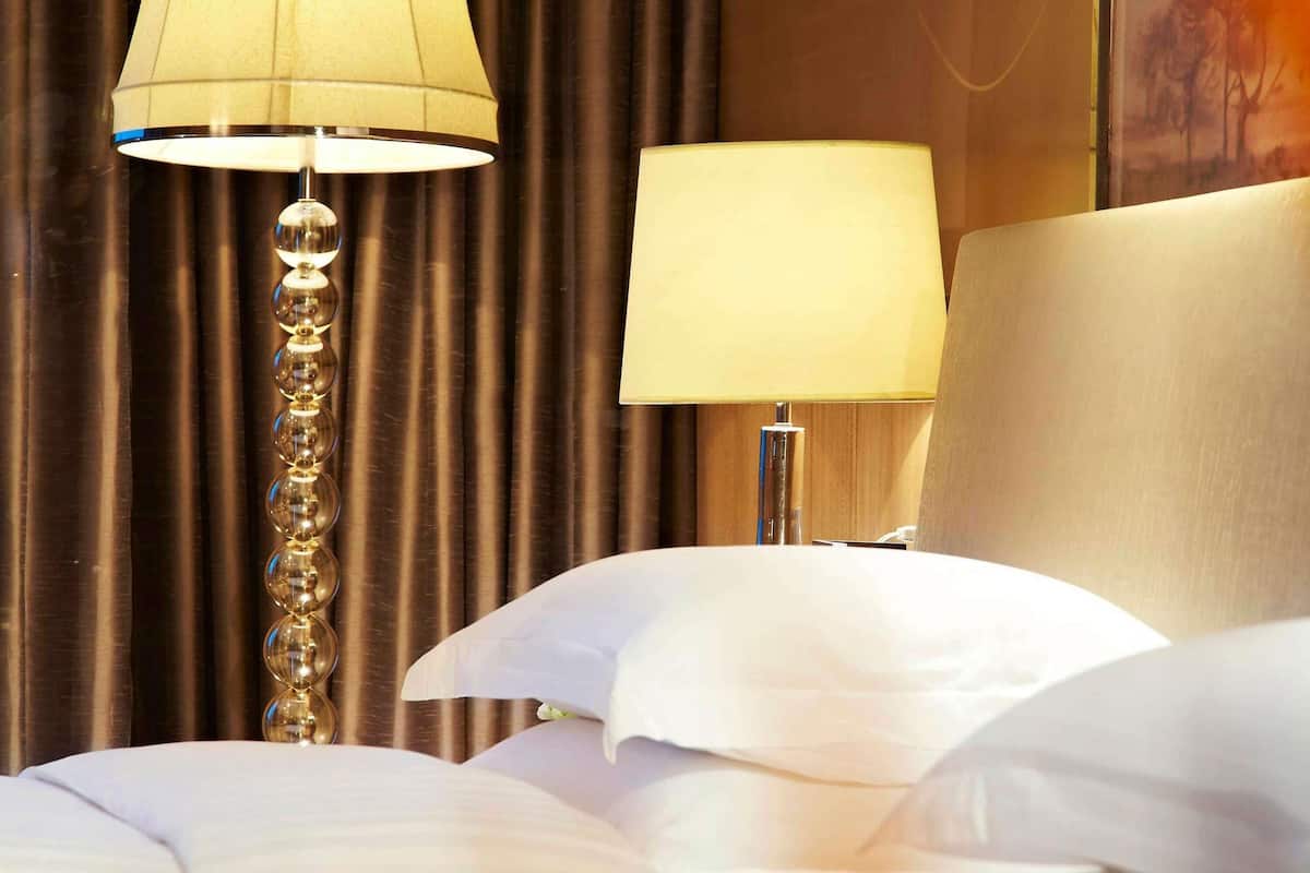 A hotel room with a bed, two bedside lamps, and a curtain backdrop.