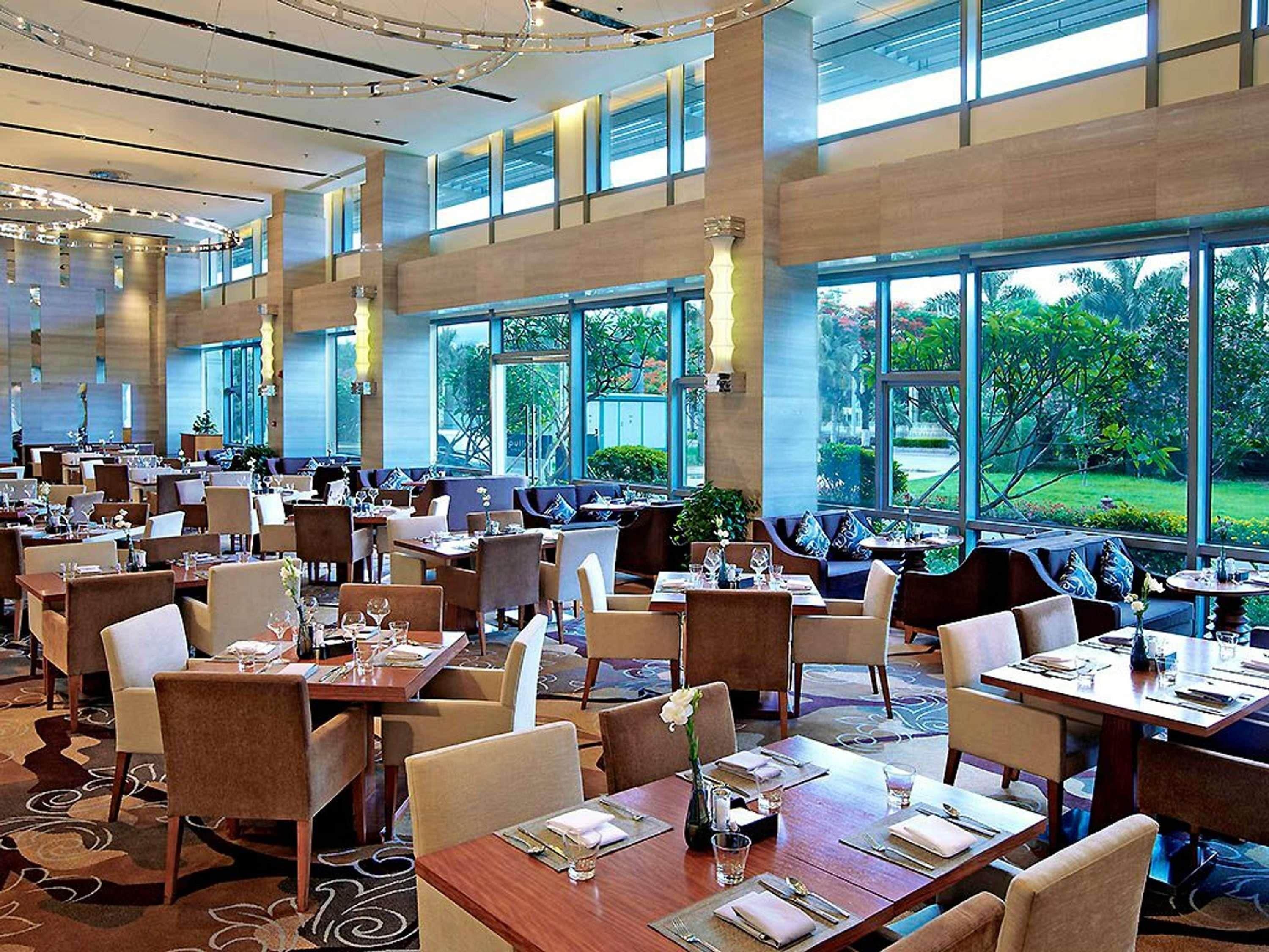 A spacious restaurant with multiple dining tables and chairs, large windows offering a view of the outdoors, and a modern interior design.