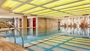 A large indoor swimming pool with a tiled floor, a glass railing, and a ceiling with recessed lighting. - Pullman Xiamen Powerlong (Xiamen)