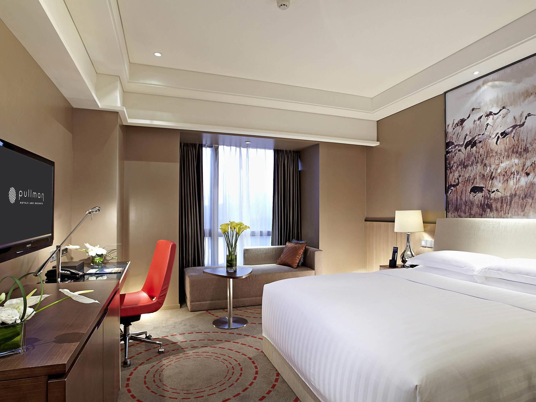 Una habitación de hotel con una cama, un escritorio, una silla, un televisor, un sofá y un cuadro en la pared.
