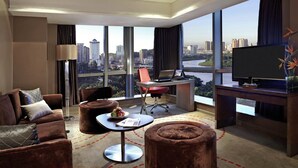 A modern hotel room with a large window offering a city view, a comfortable sofa, a desk with a laptop, and a flat-screen TV. - Pullman Xiamen Powerlong (Xiamen)
