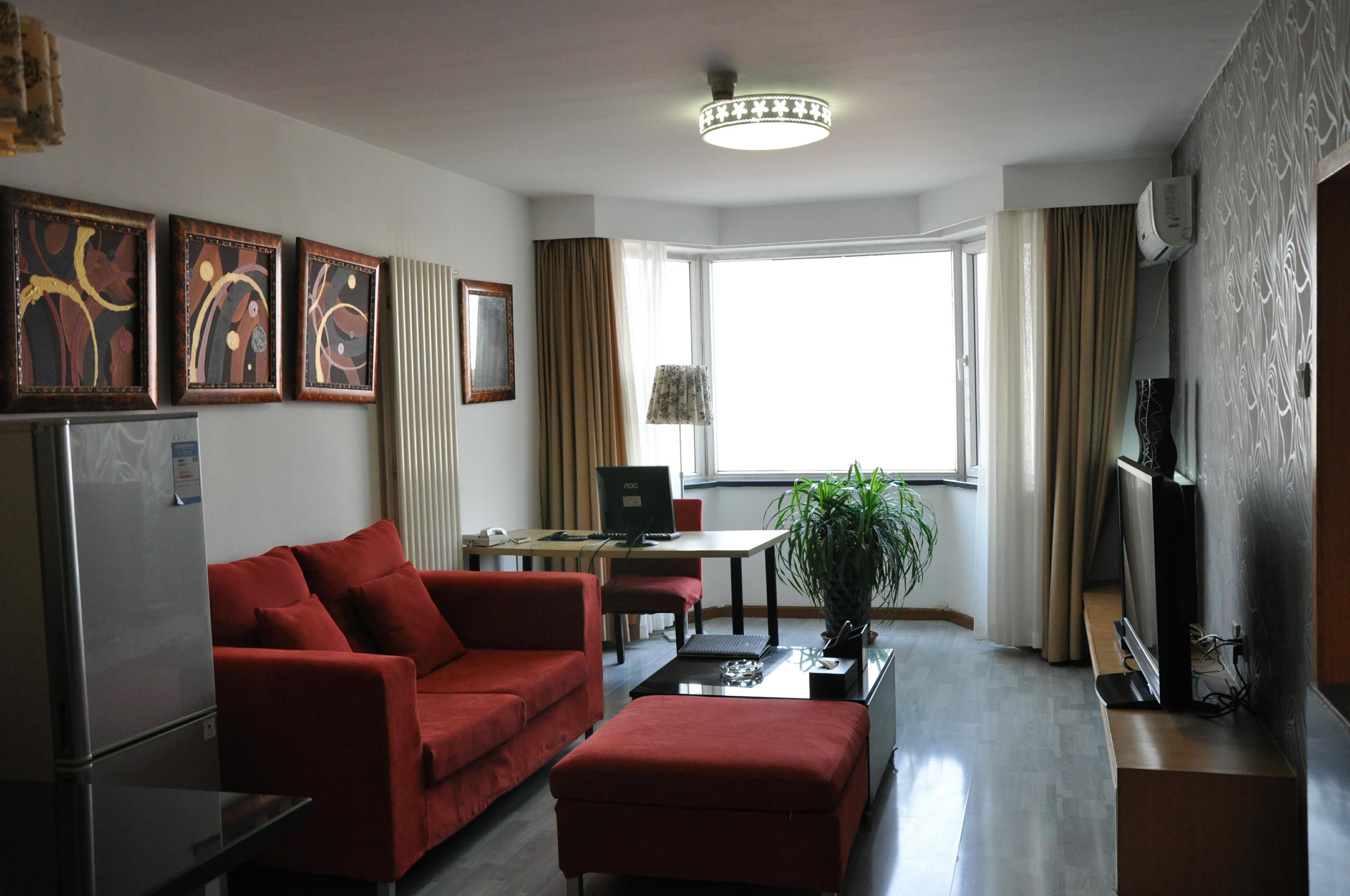 A modern living room with a red sofa, a coffee table, a TV, and a large window with curtains.