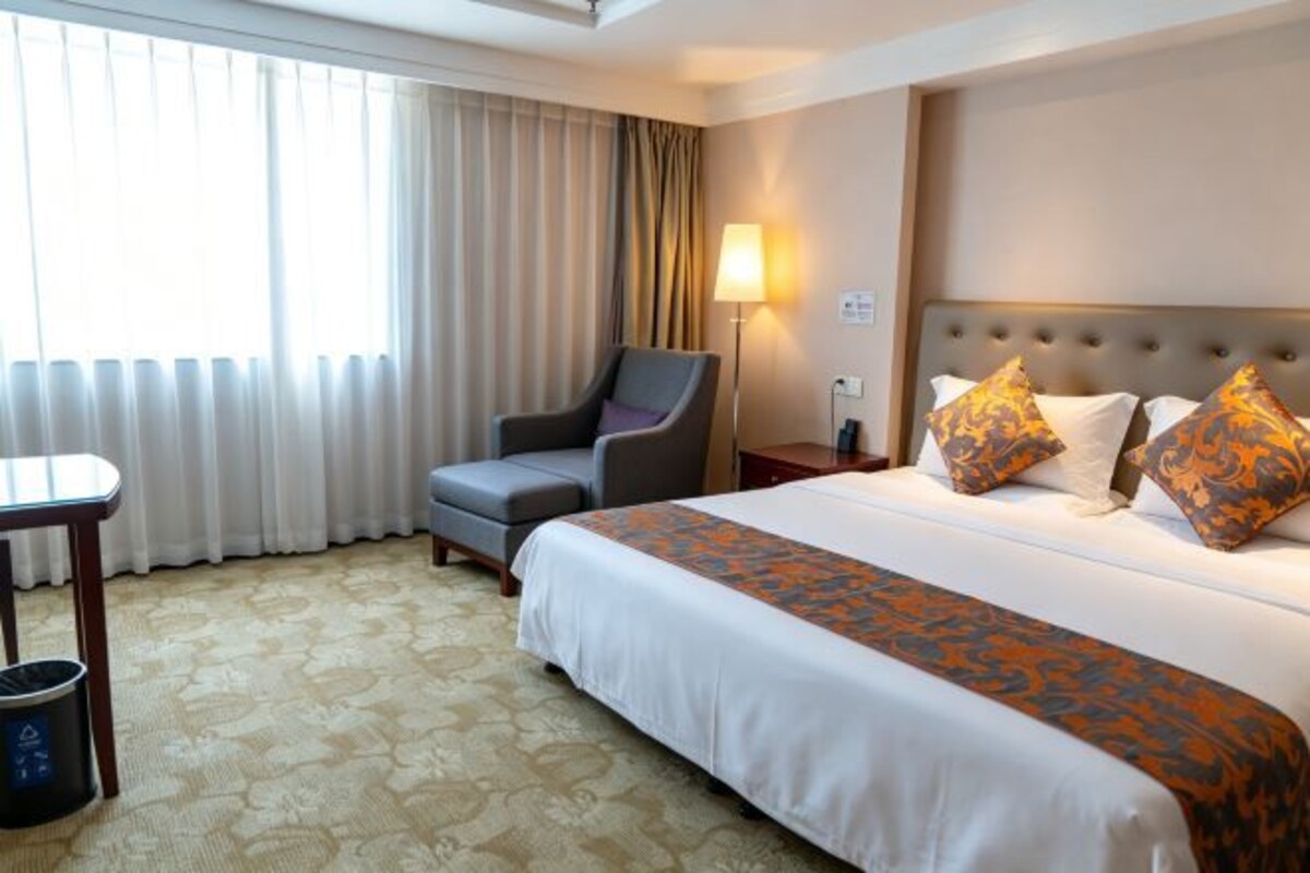 A hotel room with a bed, a desk, a chair, a lamp, and a window with curtains.