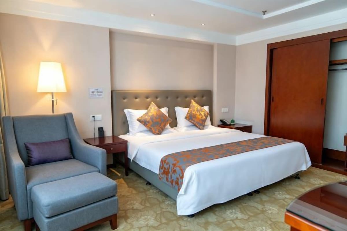 Una habitación de hotel con cama, una silla, mesita de noche, lámpara y armario.