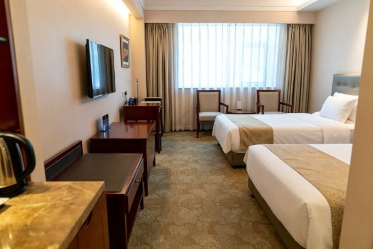 A hotel room with two beds, a desk, a television, and a window with curtains.