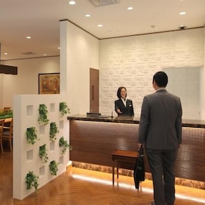 A reception area with a wooden reception desk, a receptionist, and a man in a suit. - Odakyu Station Hotel Hon-Atsugi (Atsugi)