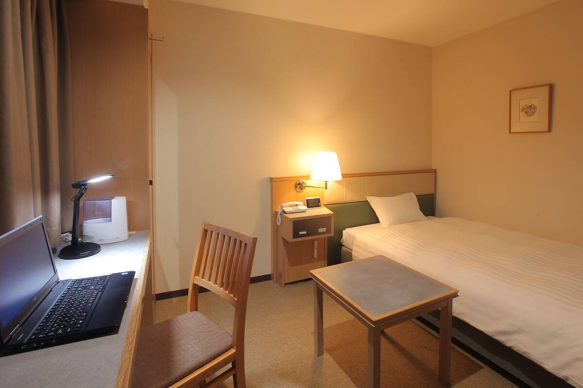 Une chambre d’hôtel comprenant un lit, un bureau avec un ordinateur portable, une chaise, une table de chevet, une lampe et une petite table de nuit.