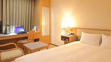 Une chambre d’hôtel avec un lit, un bureau avec un ordinateur portable, une chaise, une table de chevet avec une lampe et une fenêtre avec des rideaux.