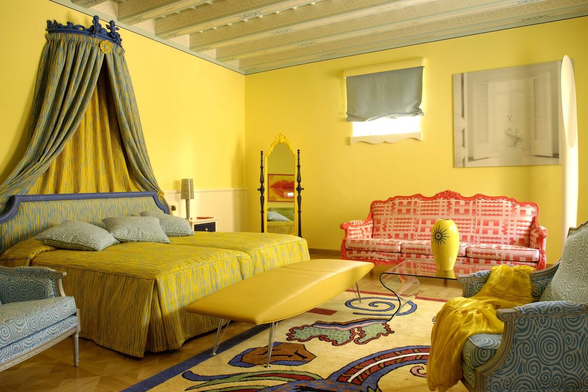 A room with a bed, a sofa, a chair, a mirror, and a window.