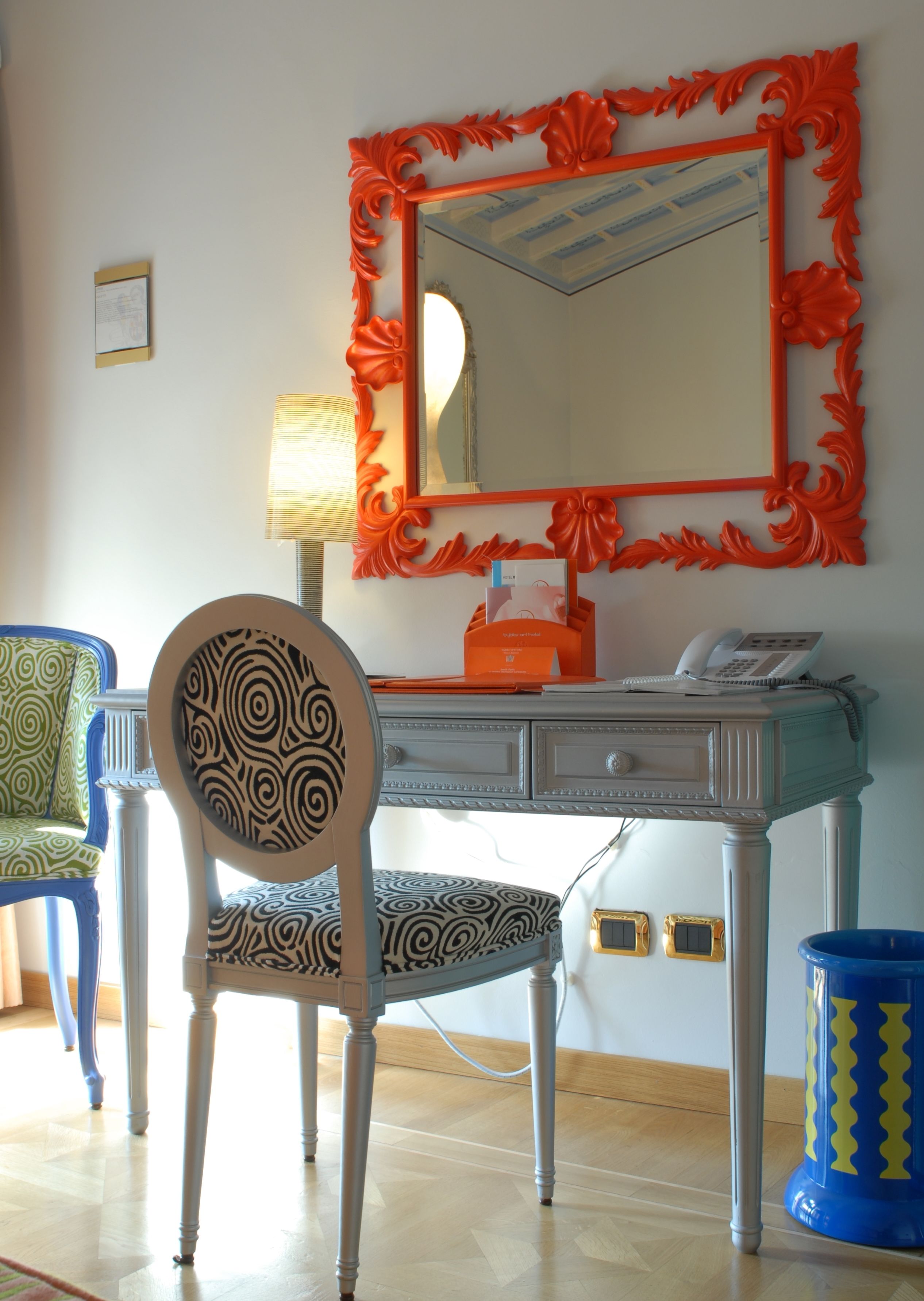 A room with a desk, a chair, a mirror, and a lamp.