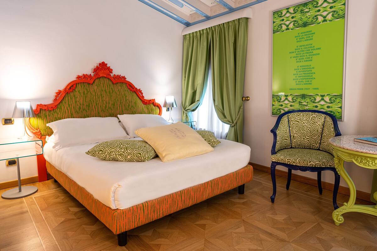 A neatly made bed with patterned pillows, a green and orange headboard, and a green curtain.