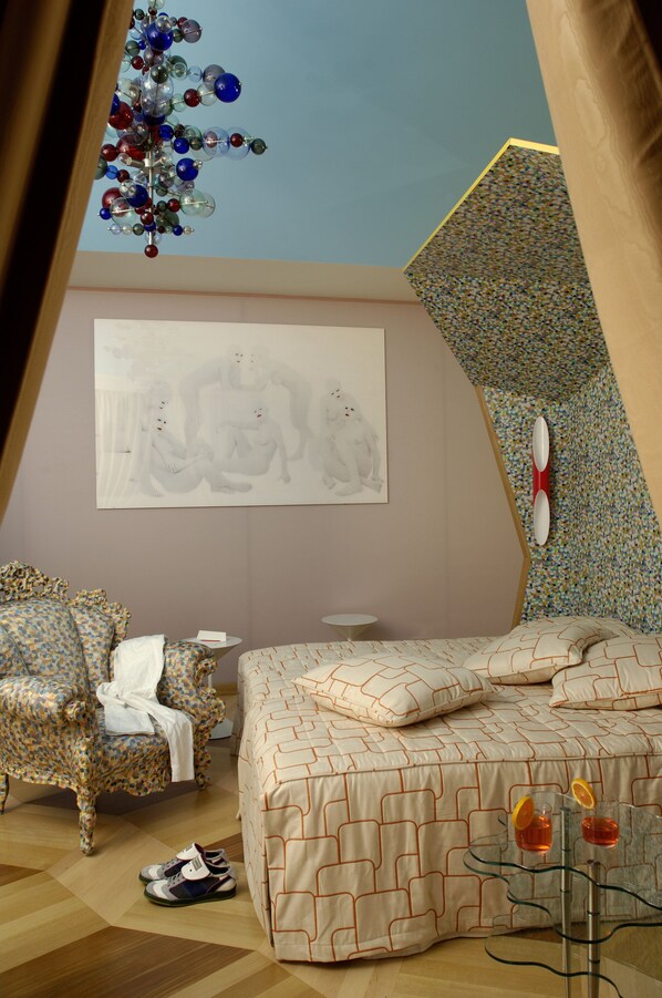A bedroom with a bed, a chair, a small table, and a unique ceiling design.