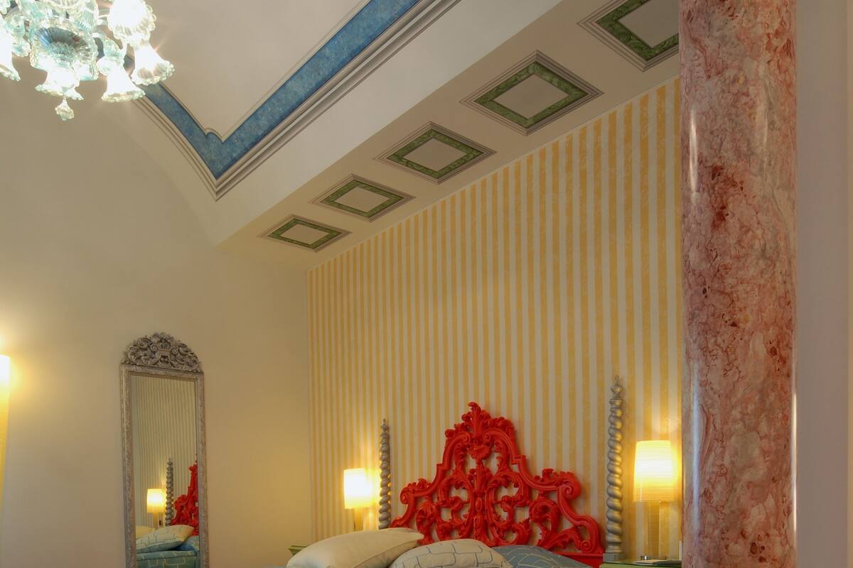 A bedroom with a bed, bench, mirror, and decorative elements.