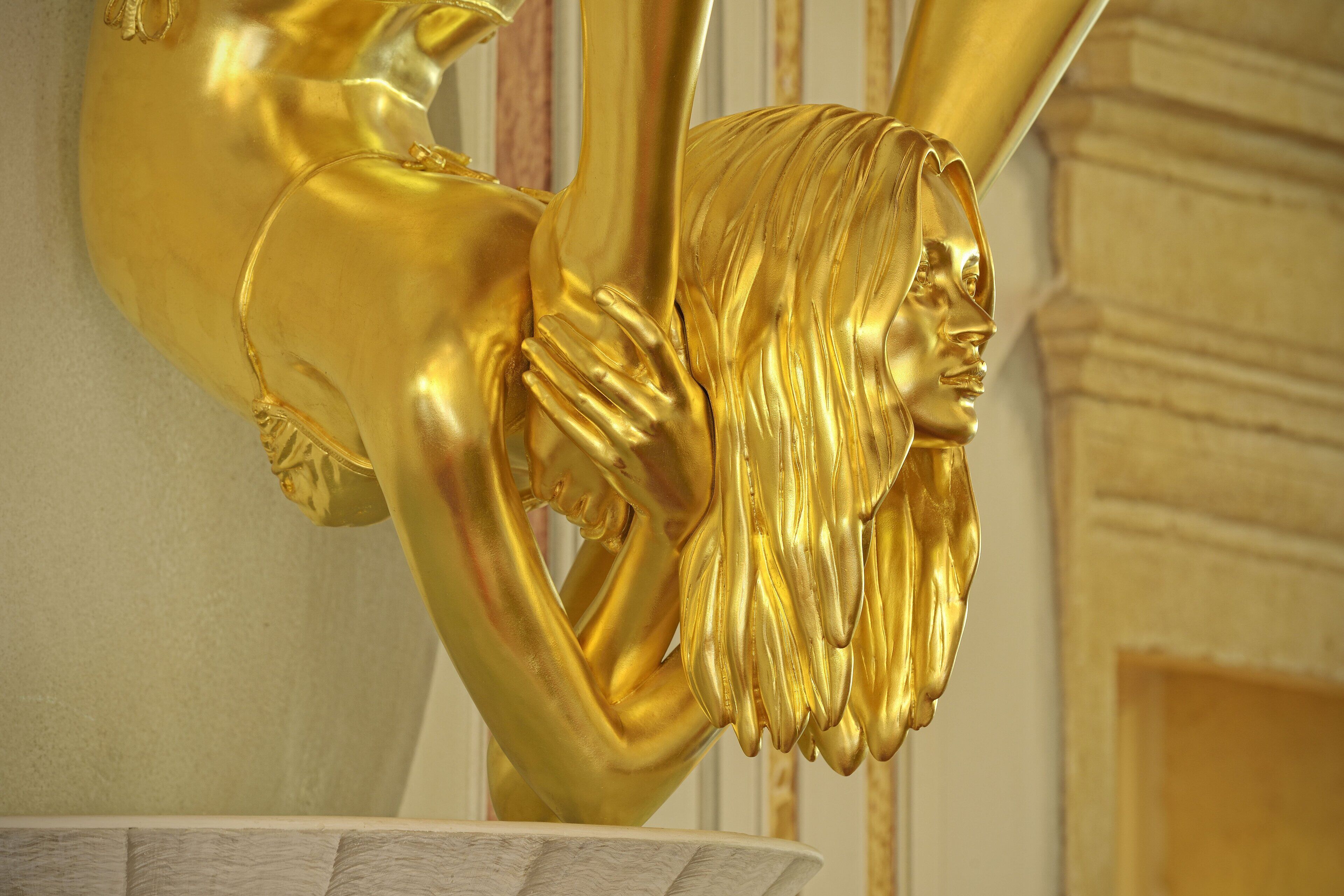 Een gouden beeld met een gedetailleerd gezicht en golvend haar, geplaatst boven een marmeren wasbak.