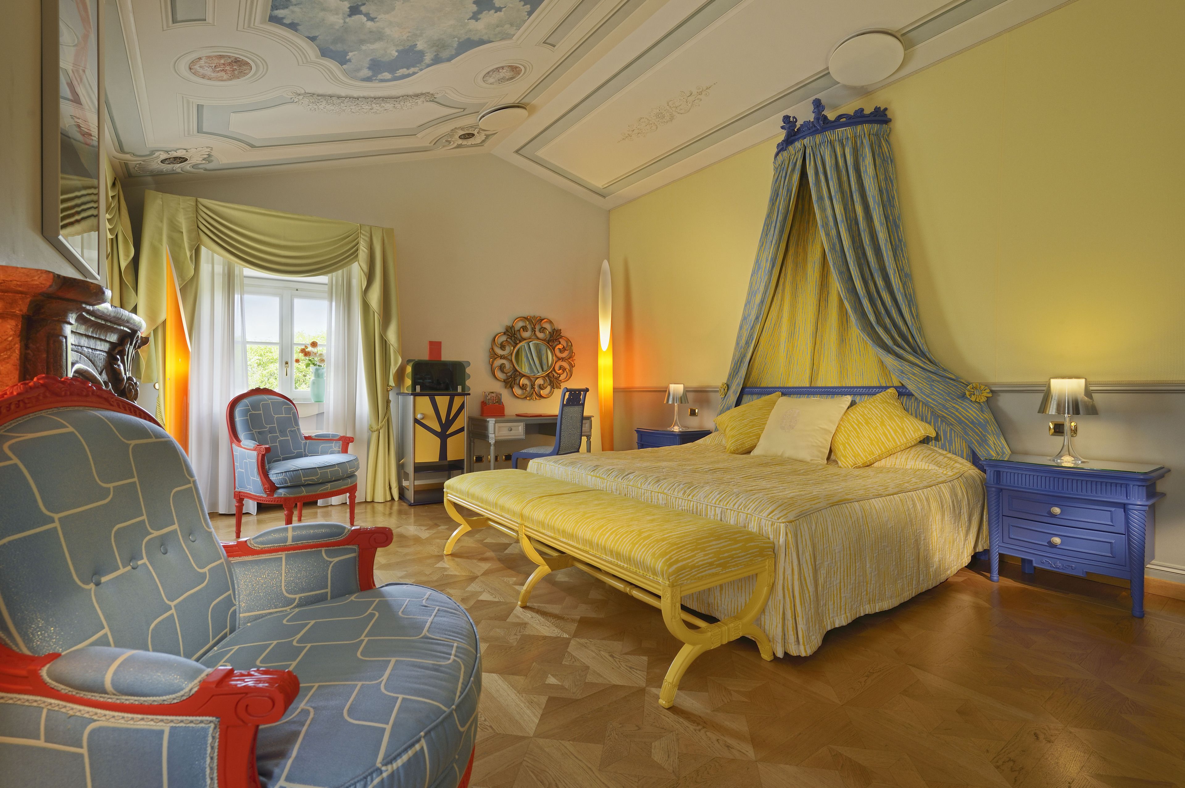 A bedroom with a large bed, a chair, a bench, a nightstand, and a mirror.