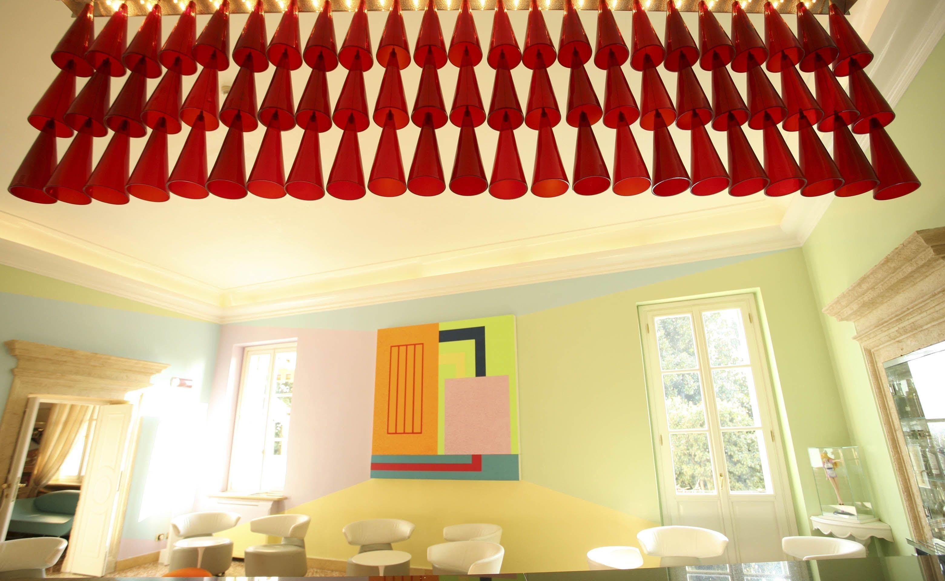 Una habitación con techo decorado con elementos cónicos rojos, un ventanal grande y una obra de arte abstracta y colorida en la pared.