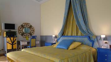 A bedroom with a four-poster bed, a television, a mirror, and a desk with a lamp.