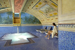 Un spa con una bañera de hidromasaje grande, paredes de azulejos azules y un techo con diseños intrincados.