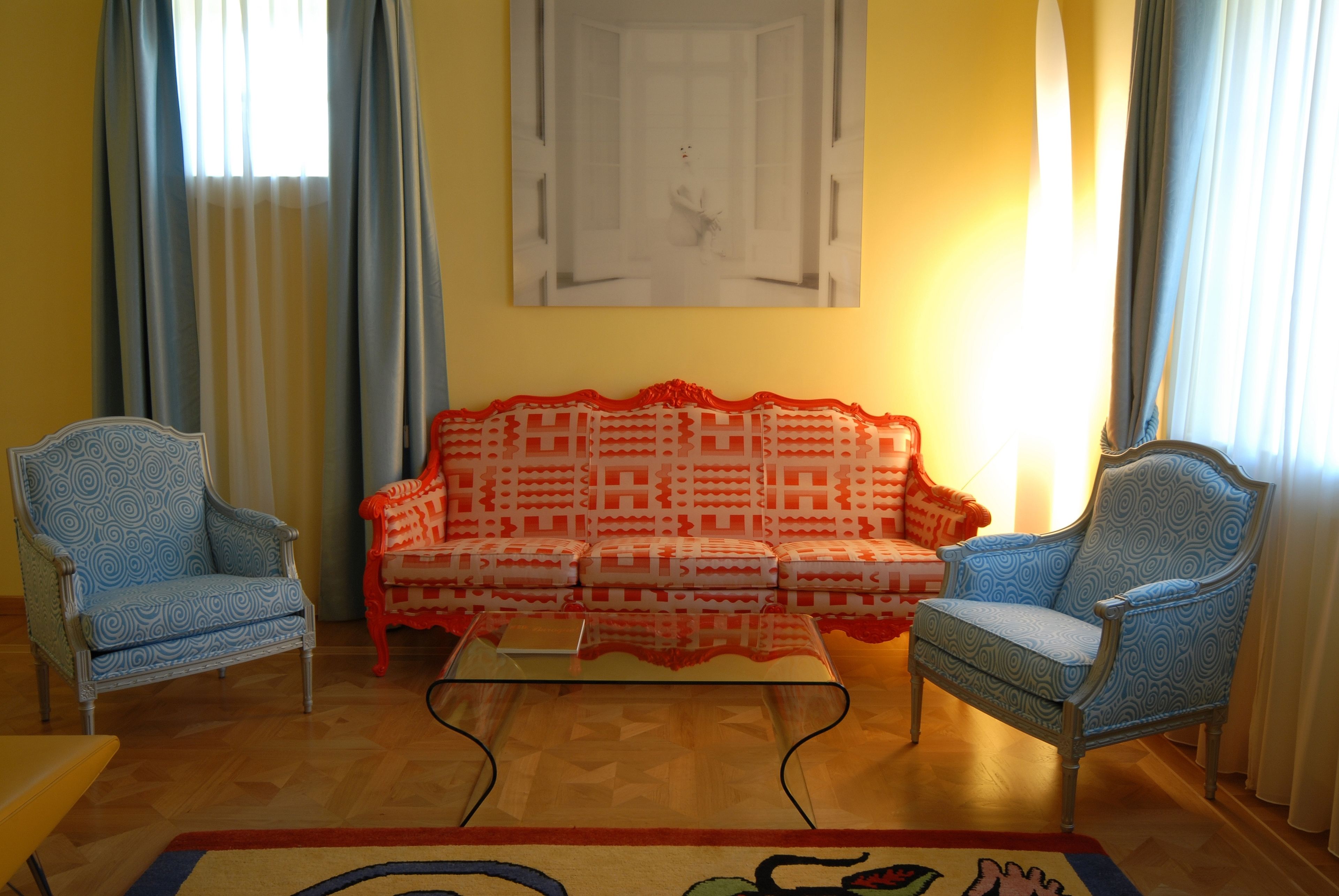 A living room with a patterned sofa, two patterned armchairs, a glass coffee table, and a rug.
