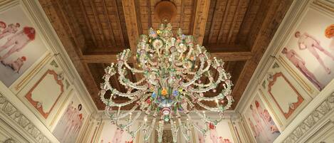 A grand room with a large chandelier, ornate ceiling, and classical wall paintings.