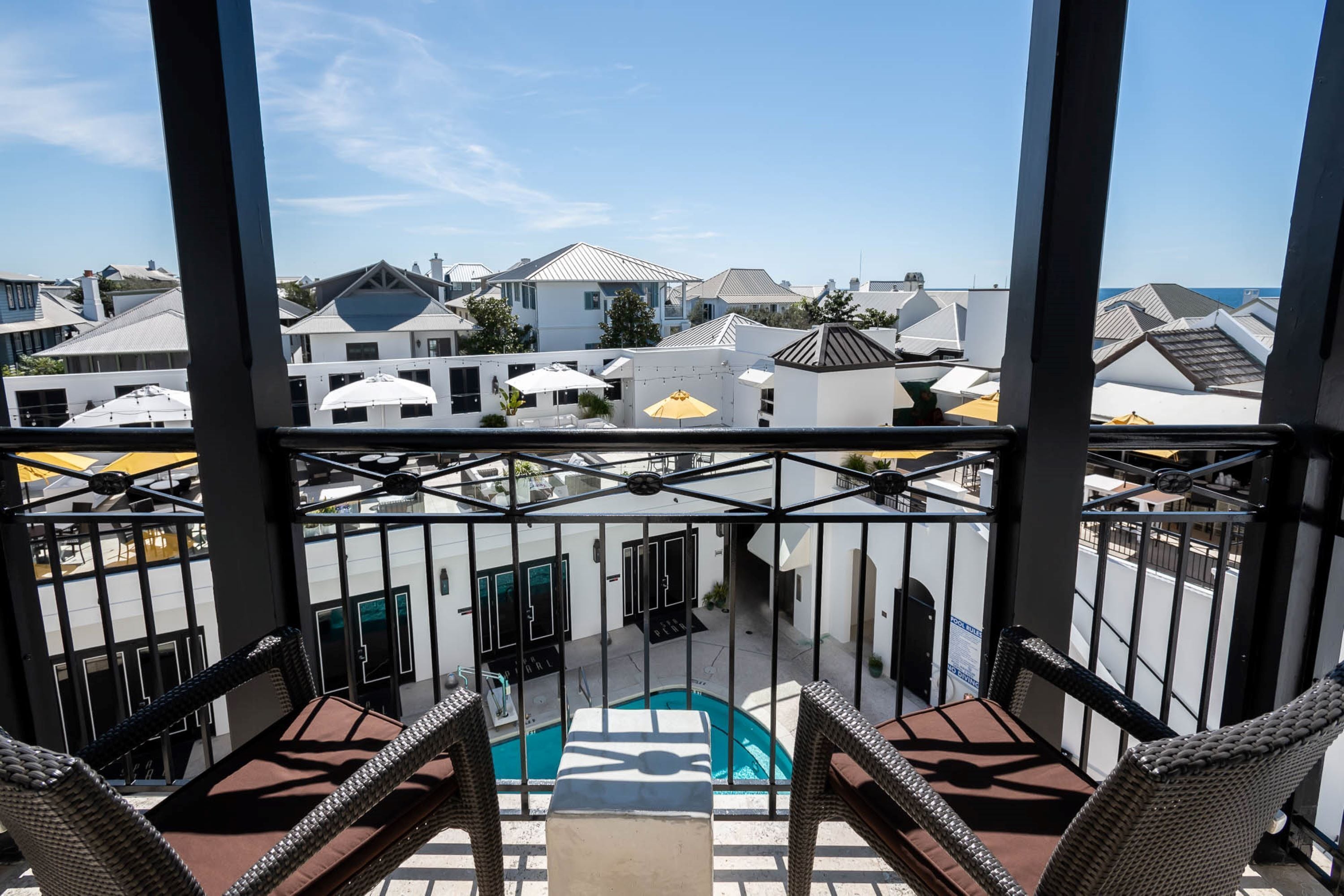 A balcony with wicker chairs, a pool, and a view of white buildings.