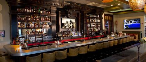 Eine Bar mit mehreren Regalen voller Spirituosenflaschen, einem an der Wand montierten Fernseher und einer Bar mit Hockern.
