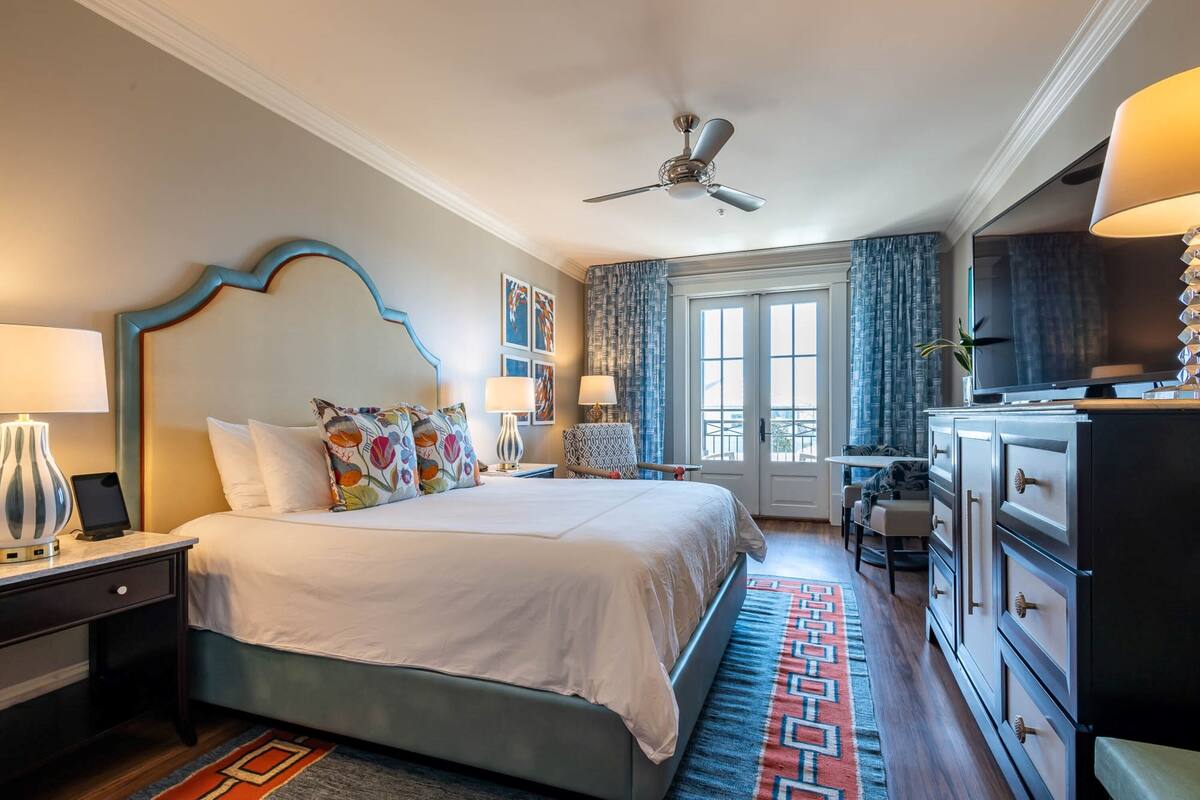 A hotel room with a large bed, a desk, a dresser, and a television.