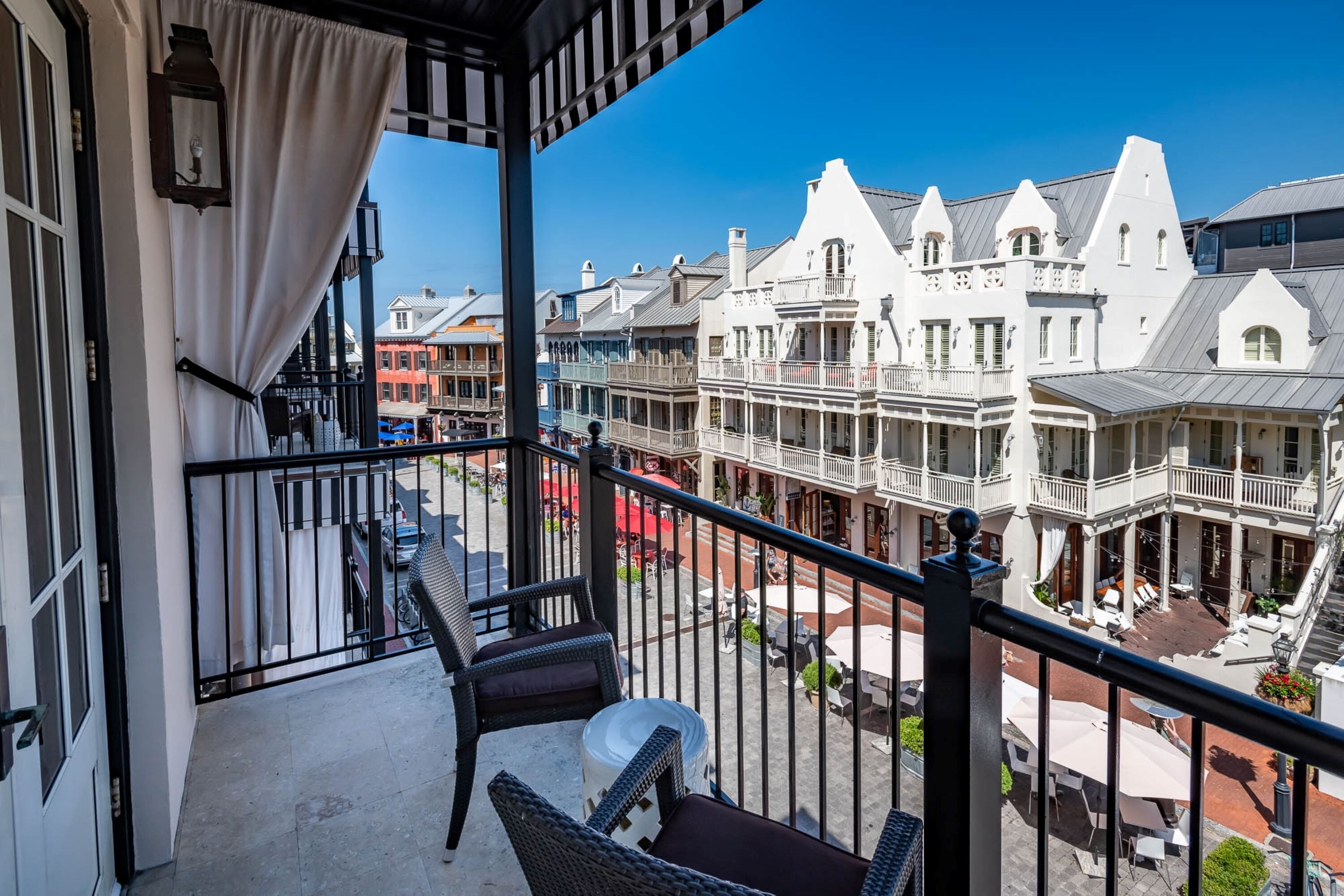 A balcony with wicker furniture, a view of historic buildings, and a clear blue sky.