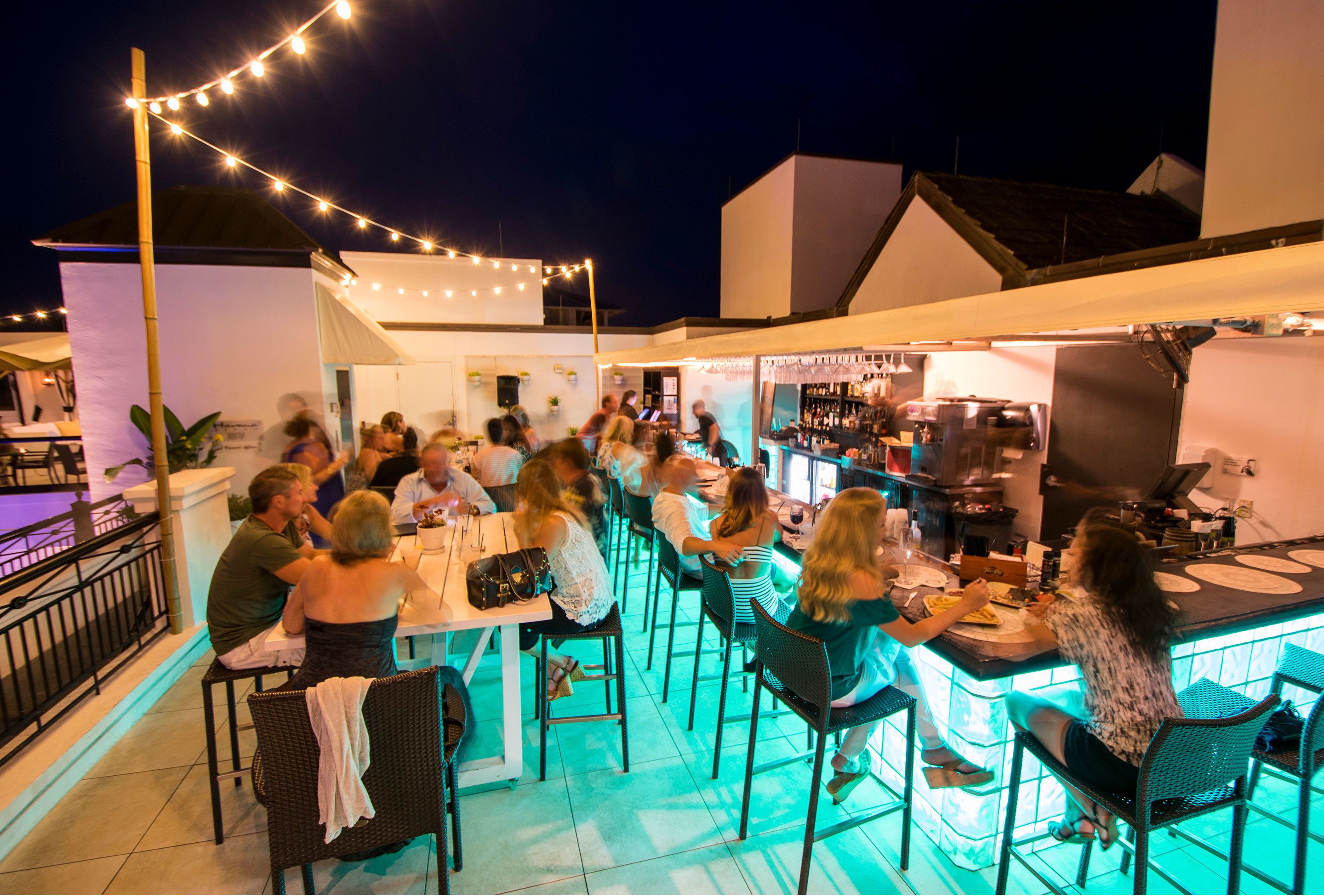 An outdoor bar area with string lights, tables, and chairs.