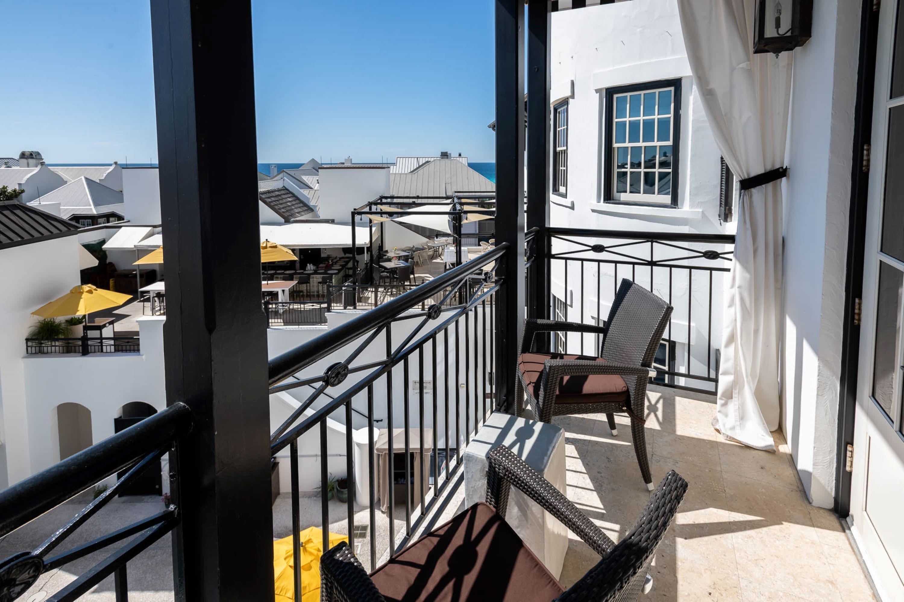 A balcony with wicker furniture, a view of the sea, and white buildings in the background.